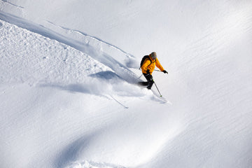 Skier carving a turn down a snowy mountain slope in bright winter light
