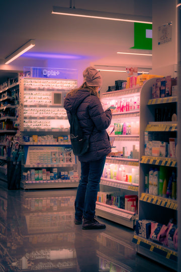 Shopper standing in a pharmacy aisle comparing products and prices on the shelves