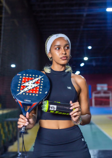 Padel player in ready position on an indoor court holding a racket and ball