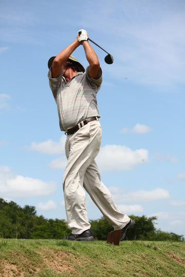 Golfer in a checked polo finishing a full swing with a driver on a sunny course