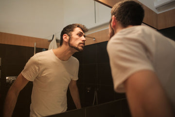 Man checking his nose in a bathroom mirror, the way you check a nasal strip reaches the sides of a wide or flat nose