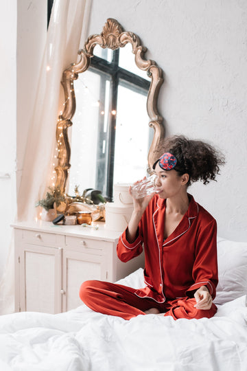 Woman sitting on her bed at night drinking a glass of water after waking with a dry mouth