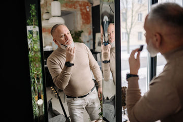 Bearded man grooming his beard in a mirror, the kind of face a nasal strip still fits because it sits above the beard line