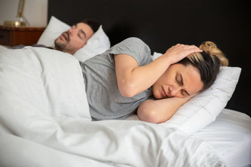 Woman lying awake and frustrated in bed while her partner snores beside her
