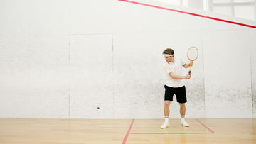 Squash player mid swing on an indoor court reaching for the ball