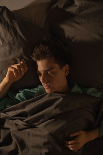 Man sleeping soundly in a dimly lit bedroom, breathing through his nose after switching from Breathe Right to an alternative nasal strip