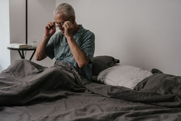 Man sitting up in bed adjusting his glasses, the moment a glasses wearer takes them off and a night nasal strip takes over