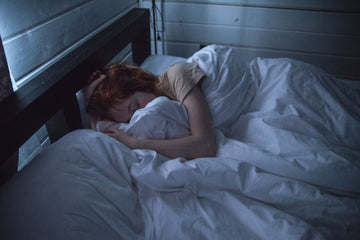 Woman asleep in white bedding at night, the scenario a nasal strip has to survive for a full eight hours